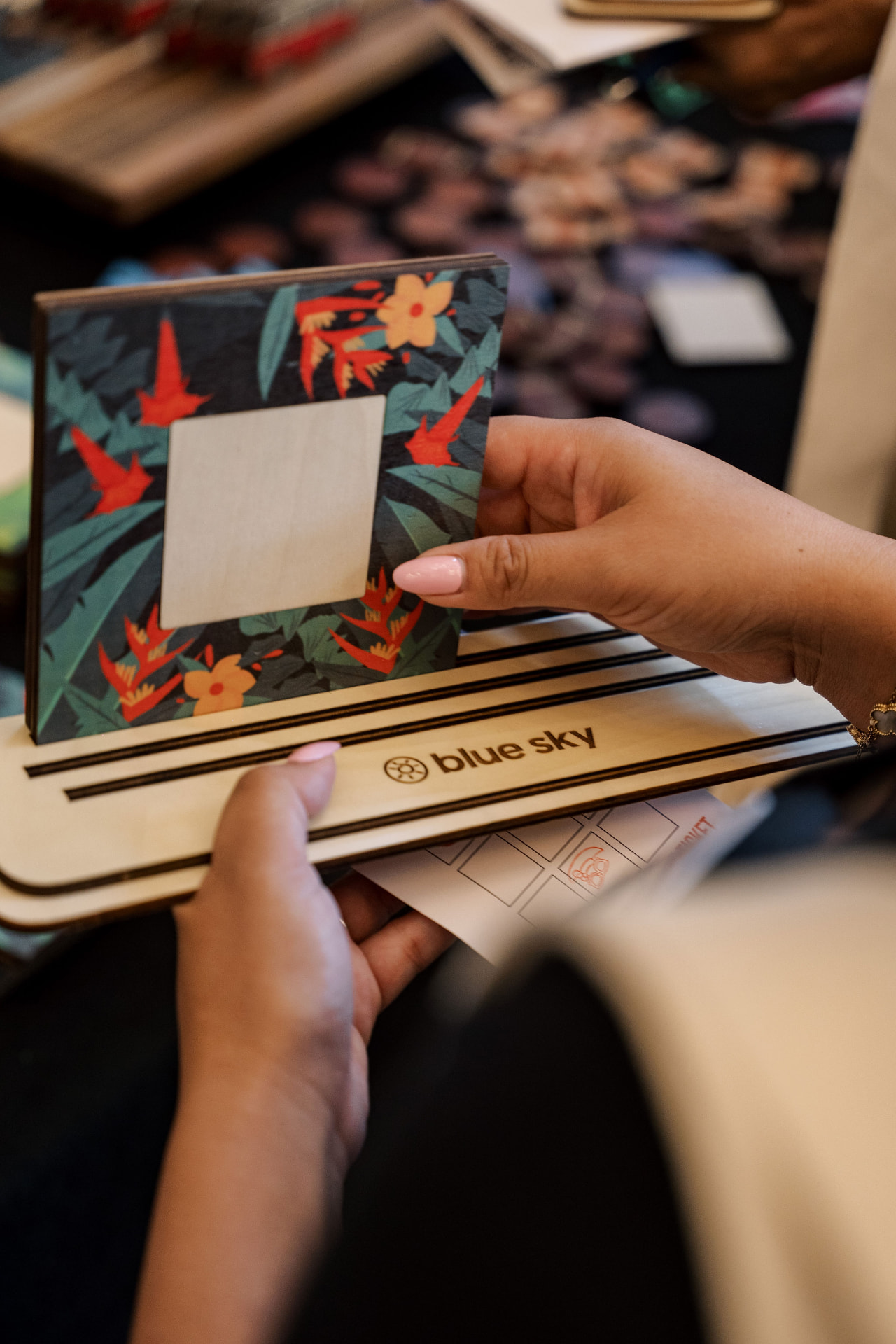 Hands placing a floral picture frame on a Blue Sky branded wooden base