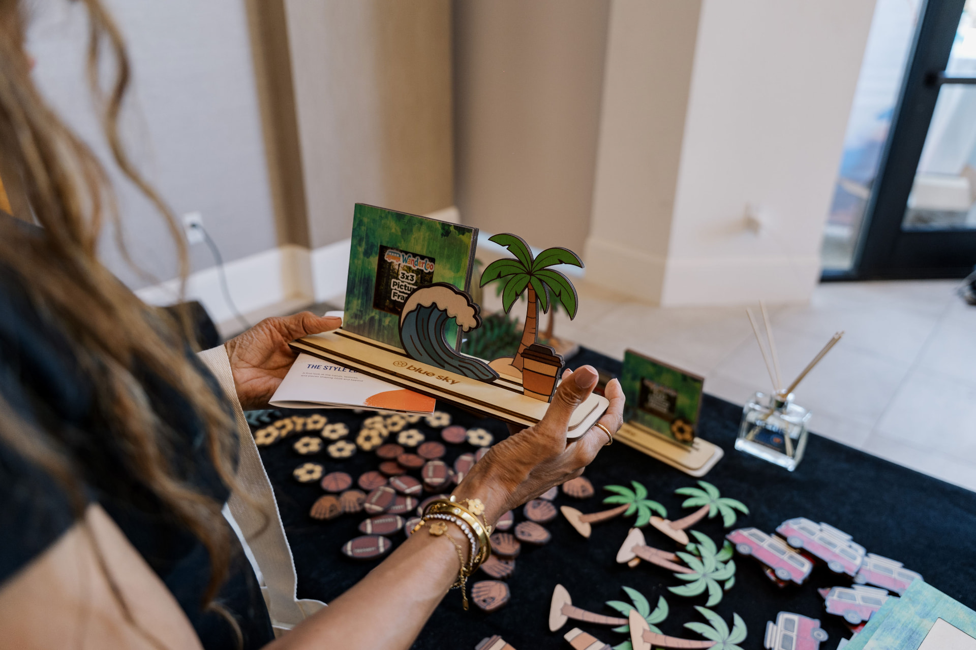 Guest personalizing a picture frame with wave and palm tree charms at a table of decorative pieces